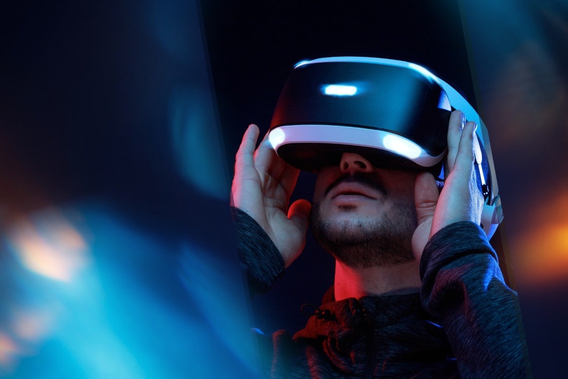 A bearded man enjoying a virtual‑reality experience with VR goggles in one of Barcelona’s innovative tech spaces. He holds the headset with both hands.