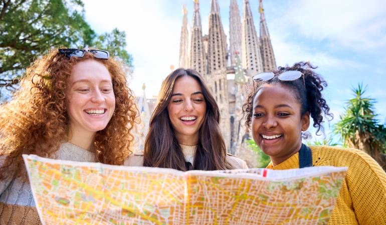 Thre young woman looking at a map in front the Sagrada Família.