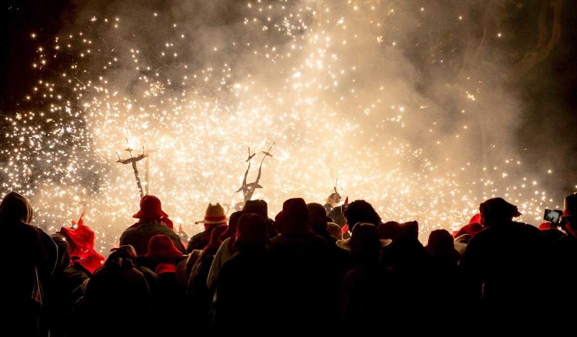 Vistes del correfoc darrere d'un grup gran de gent entre la qual es veuen les guspires dels petards que porten els diables.