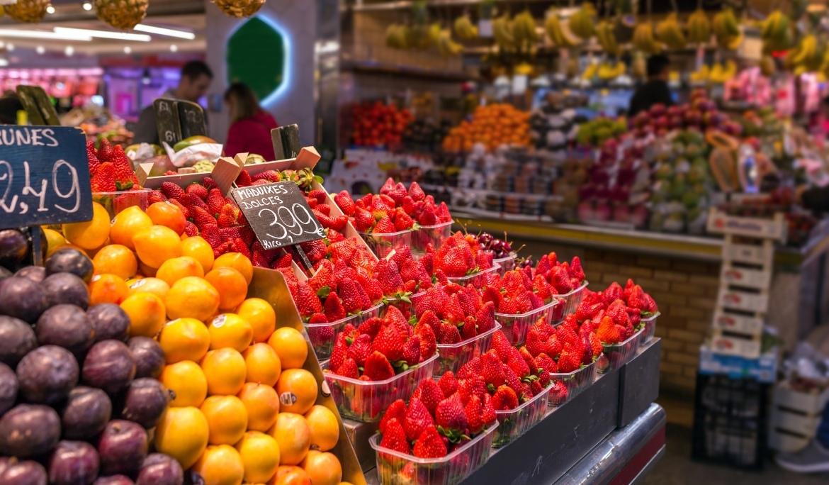 Primer pla d’una parada de fruita a un dels mercats de Barcelona, s’hi poden veure maduixes, taronges i prunes.