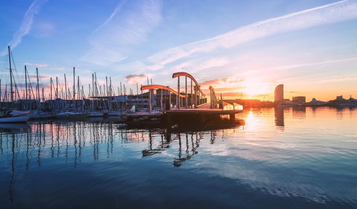 A sunset view of Port Vell in Barcelona, with the Maremagnum and the marina’s boats in the background.