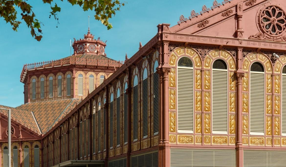 Façana modernista del edifici del Mercat de Sant Antoni vista des de un punt elevat del lateral durant un dia clar. Es veu com és un dels mercats de Barcelona més grans.