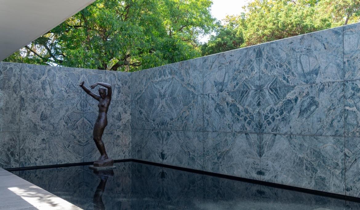 Imagen del patio interior del Pabellón Alemán, con vistas a una escultura de formas femeninas y a un estanque de agua.