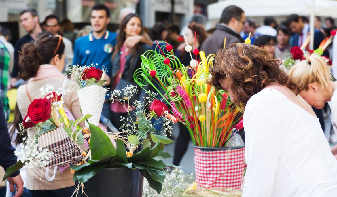 Imatge d'una parada de Sant Jordi amb flors i llibres. Hi ha molta gent que es para a mirar-la.