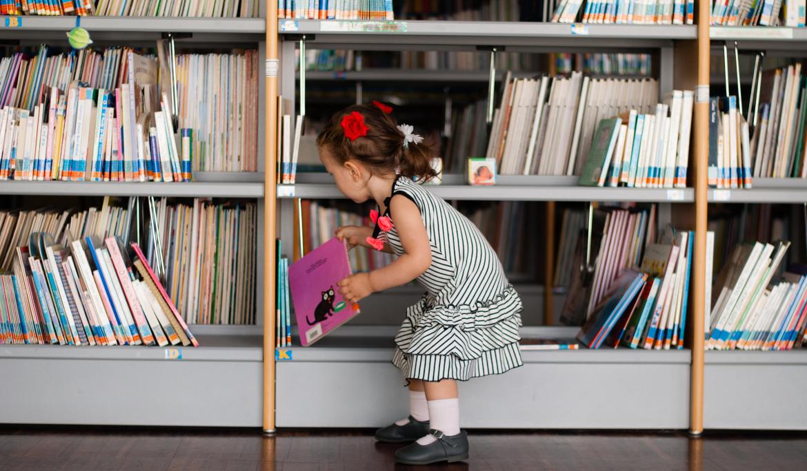 A little girl picking out a book from a library that's highly recommended for visiting Barcelona with kids.