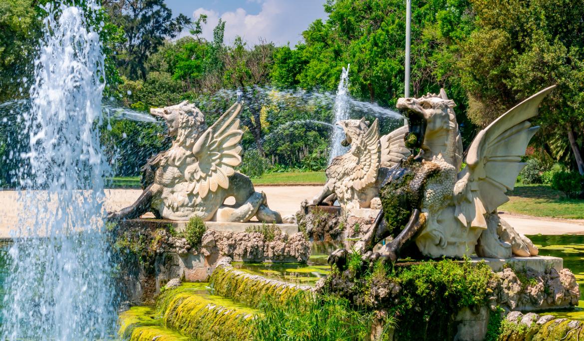 Monstrous stone water figures forming a fountain in Parc de la Ciutadella; the weather is beautiful and everything around them is green. It is a perfect spot to enjoy Barcelona with kids