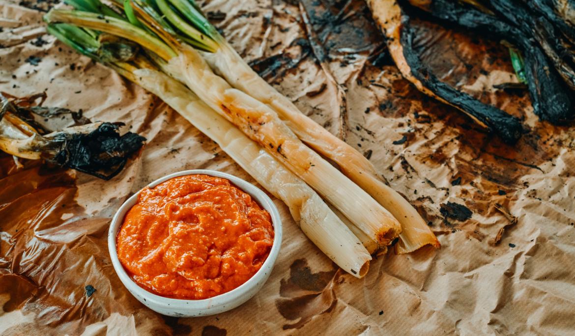 Una taula amb un manac de calçots i un bol de salsa romesco.