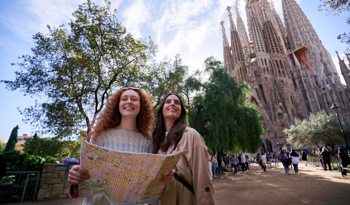 Two girls checking a city map with their backs to the Sagrada Família.