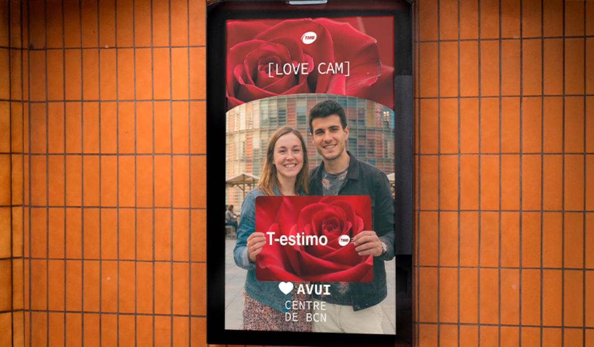 imatge d'una pantalla de l'andana del metro amb una parella aguantant una targeta gengant