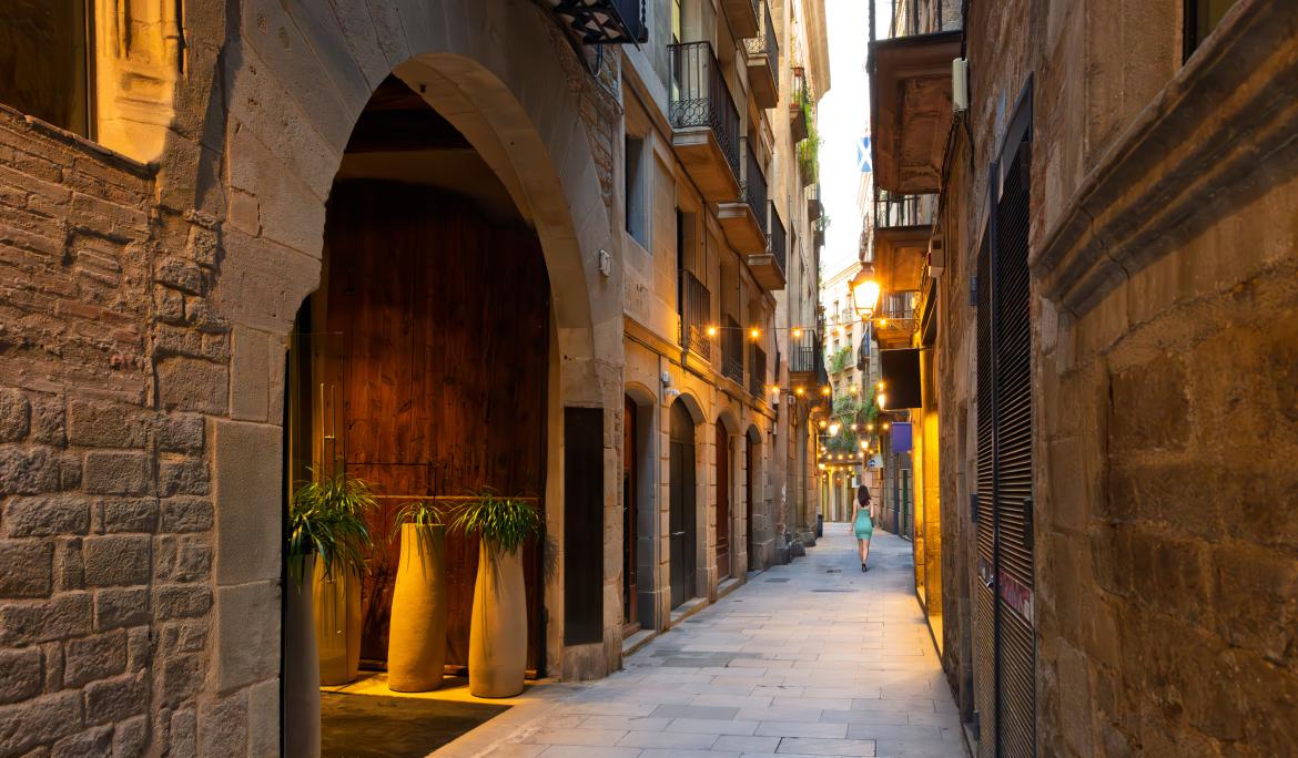 Dark alley in the Gothic Quarter with stone houses and shops.