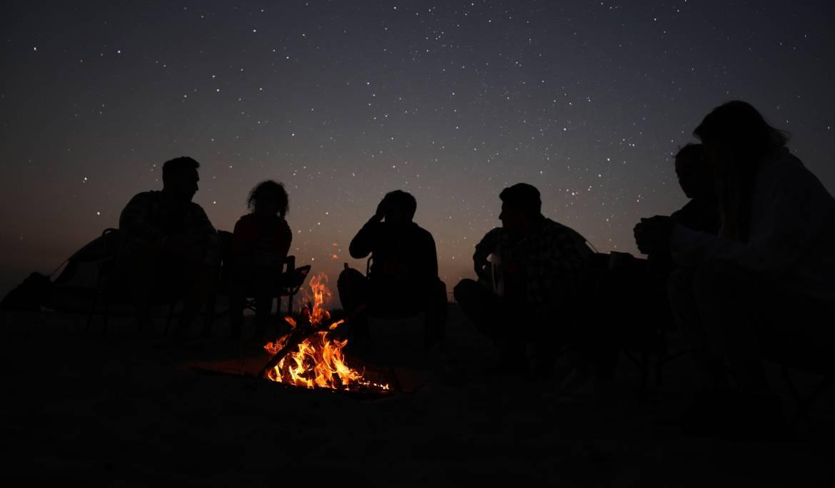 Jóvenes a contraluz iluminados por la luz de una hoguera en la playa durante una verbena de San Juan en Barcelona