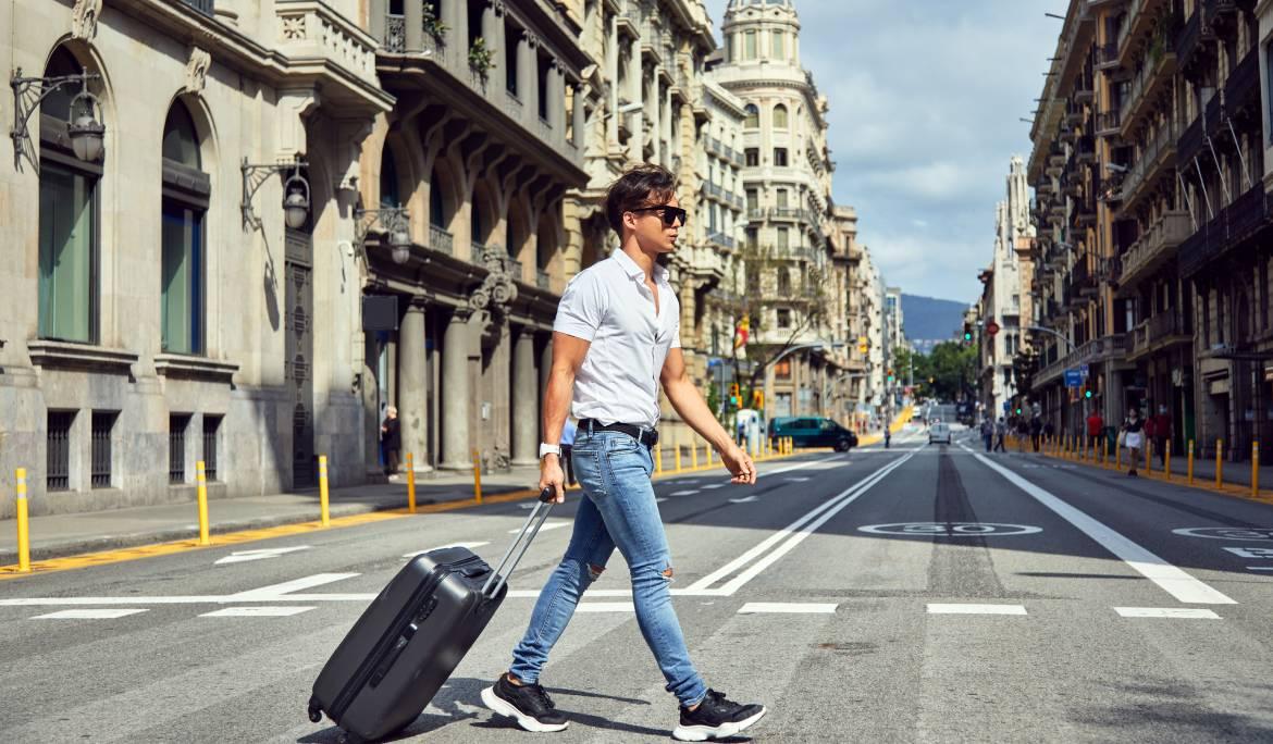 Home jove amb una maleta creuant un carrer de Barcelona