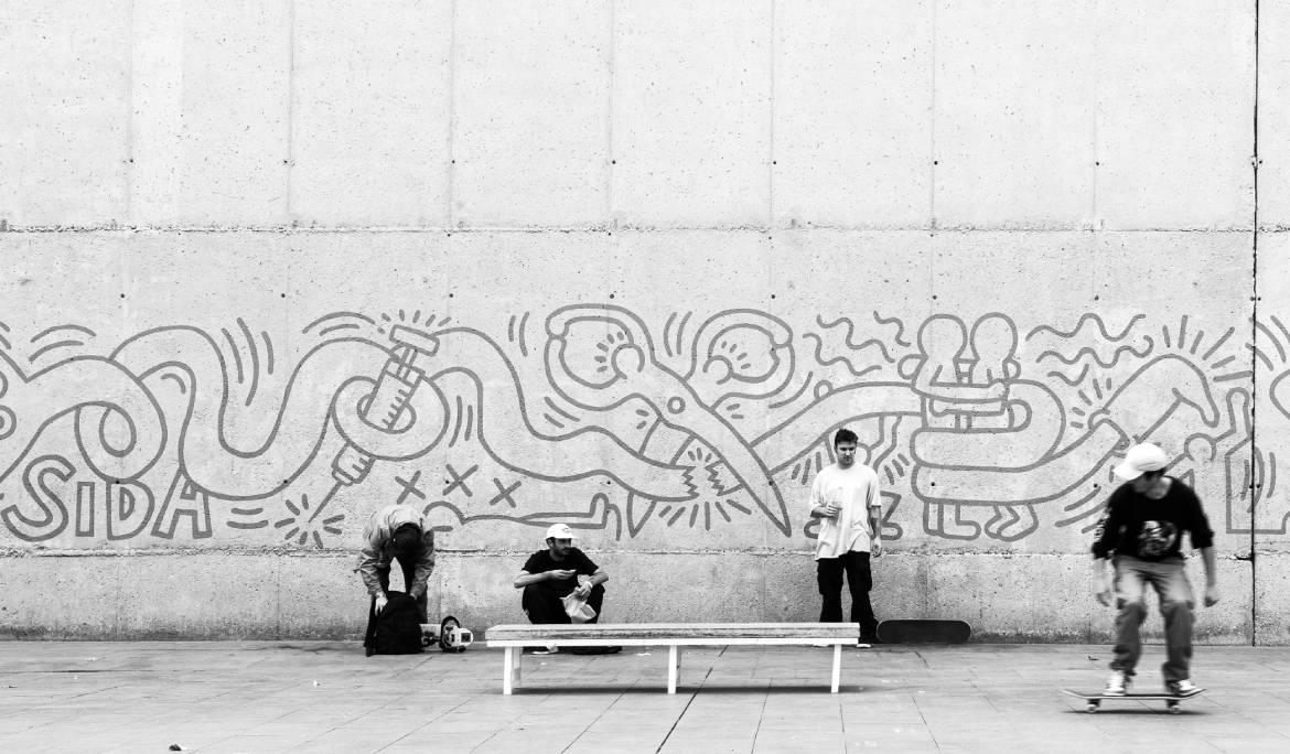 Imagen del mural del Sida con chicos jóvenes haciendo skate por los alrededores. La imagen está en blanco y negro.