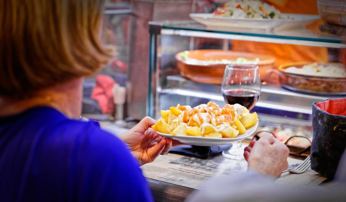 Image of a plate of patatas bravas, crispy potatoes served with spicy sauce and aioli on a wooden table