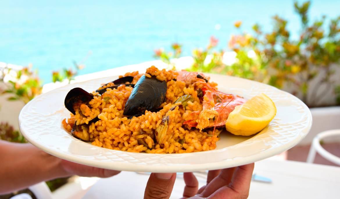 Image of a traditional seafood paella served in a pan, featuring prawns, mussels, and rice cooked to perfection.