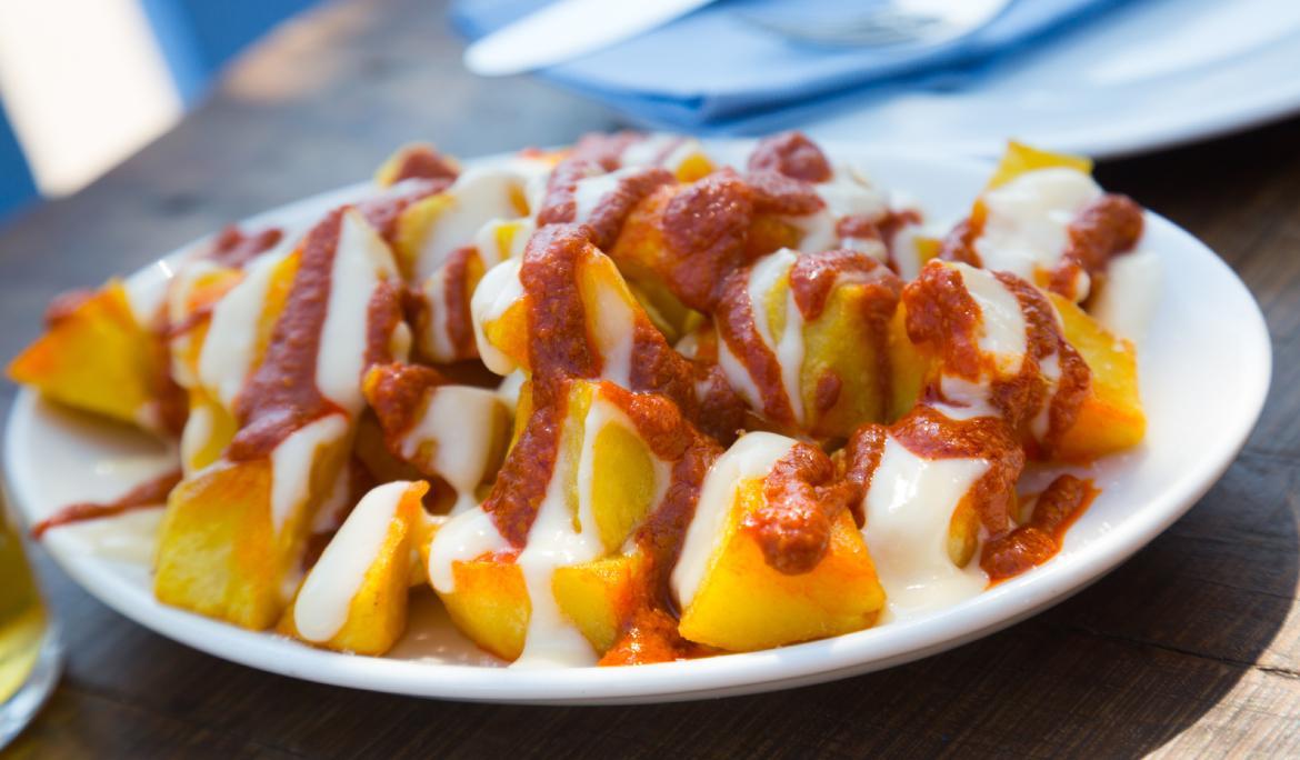 Image of a freshly cooked portion of patatas bravas with garlic aioli and spicy sauce on a table.