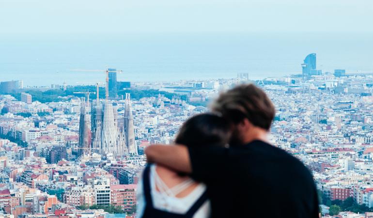 Pareja abrazada en un mirador, de espaldas a la cámara, con el skyline de Barcelona de fondo. / Foto: Kalinova Olena via Adobe Stock