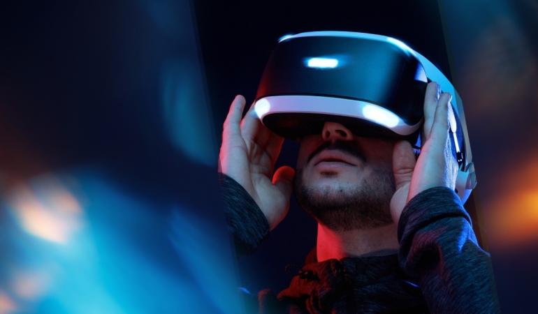 A bearded man enjoying a virtual‑reality experience with VR goggles in one of Barcelona’s innovative tech spaces. He holds the headset with both hands.
